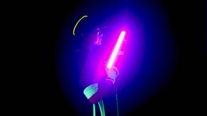 Une personne est dans le noir et tient un bâton fluorescent rose.